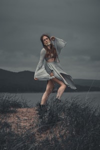 a woman in a dress is standing on a hill next to a body of water