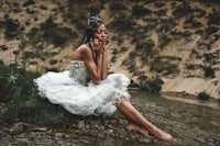 a woman in a white dress sitting on a rock in a river