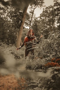 a woman in a cloak walking through the woods