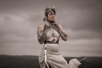 a woman with tattoos standing on a hill