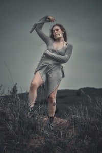 a woman in a gray dress standing on a hill