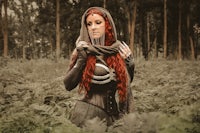 a red haired woman in a cloak standing in the woods