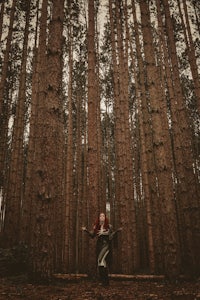 a woman standing in a forest with tall trees