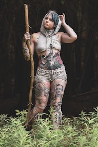 a woman with tattoos holding a stick in the woods