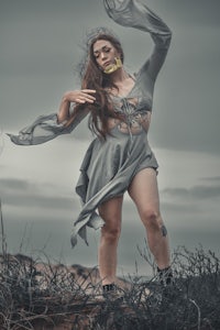 a woman in a gray dress is standing in a field