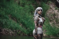 a woman with tattoos standing next to a river