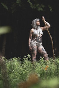 a woman with tattoos standing in the woods