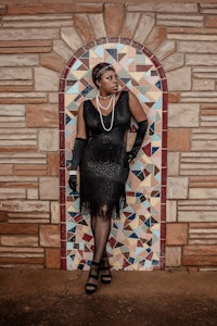 a woman in a black dress leaning against a tiled wall