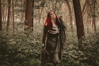 a woman with red hair standing in the woods