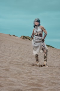 a woman with tattoos standing on a sand dune