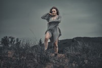 a woman in a gray dress standing on a hill