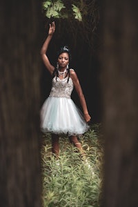 a girl in a white dress is standing in the woods